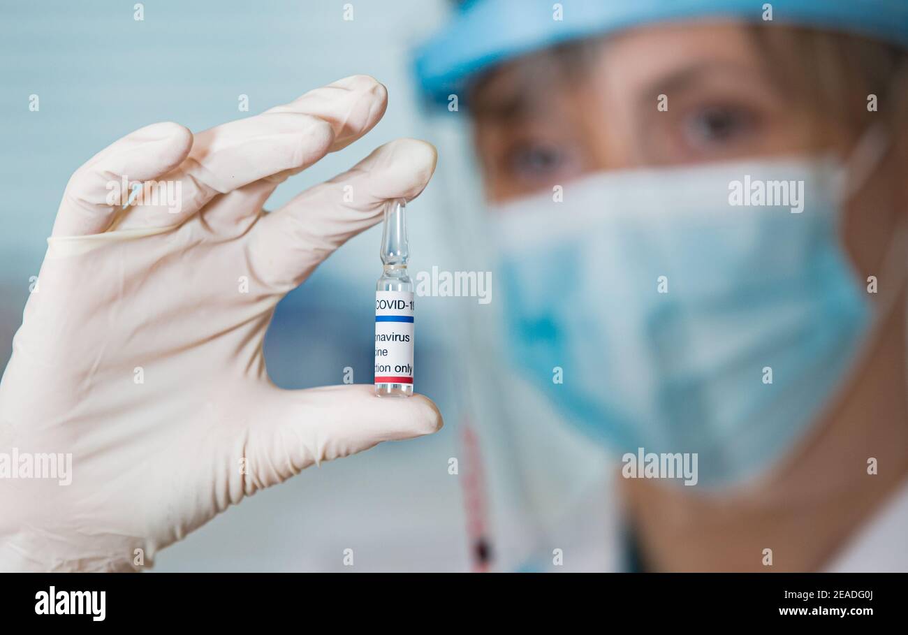 Ärztin mit OP-Maske und in Handschuhen mit Impfampulle und Spritze. Impfung während der COVID-19-Pandemie Stockfoto