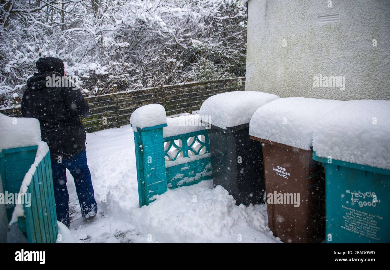 Glasgow, Schottland, Großbritannien. Februar 2021, 9th. Im Bild: Eine Person räumt einen Schnee auf einem Fußgängerweg mit einer Schneeschaufel angehäuft als Storm Darcy hat fast einen Fuß Schnee fallen über Nacht blockiert Wege und Pilling hoch auf Mauern, Tore, Wheelie-Behälter hinterlegt. In der vorherigen Nacht fiel auch Schnee, aber nicht so viel wie in der letzten Nacht. Die eisigen Temperaturen haben sich um die -1C gehalten, die letzte Nacht war die kälteste bisher. Quelle: Colin Fisher/Alamy Live News Stockfoto