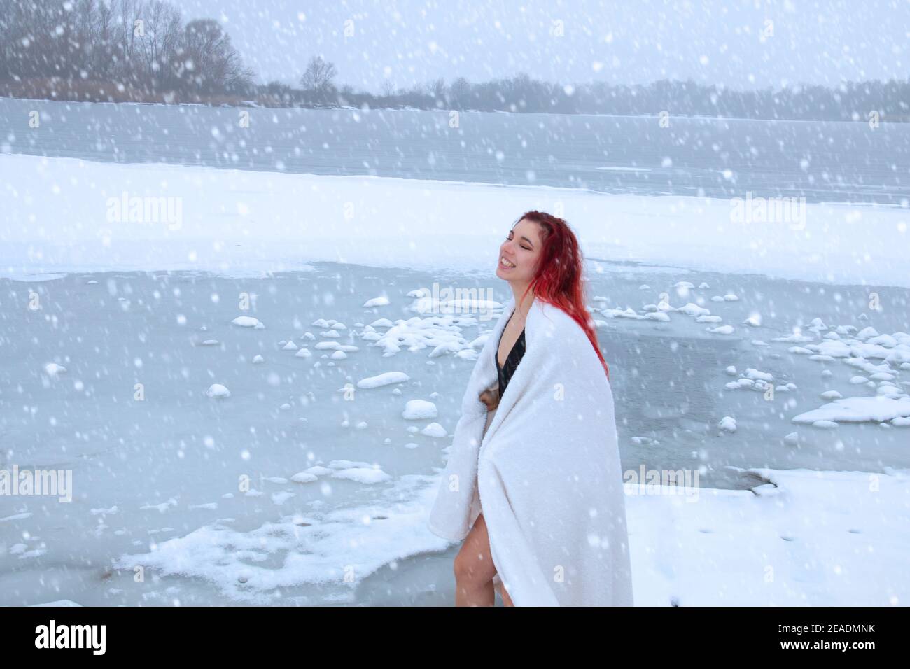 Härtende, extrem junge Frau in einem Handtuch im Freien auf Schneedusche gewickelt, Körper Kryotherapie am natürlichen See in schneebedeckten wilden Natur Stockfoto