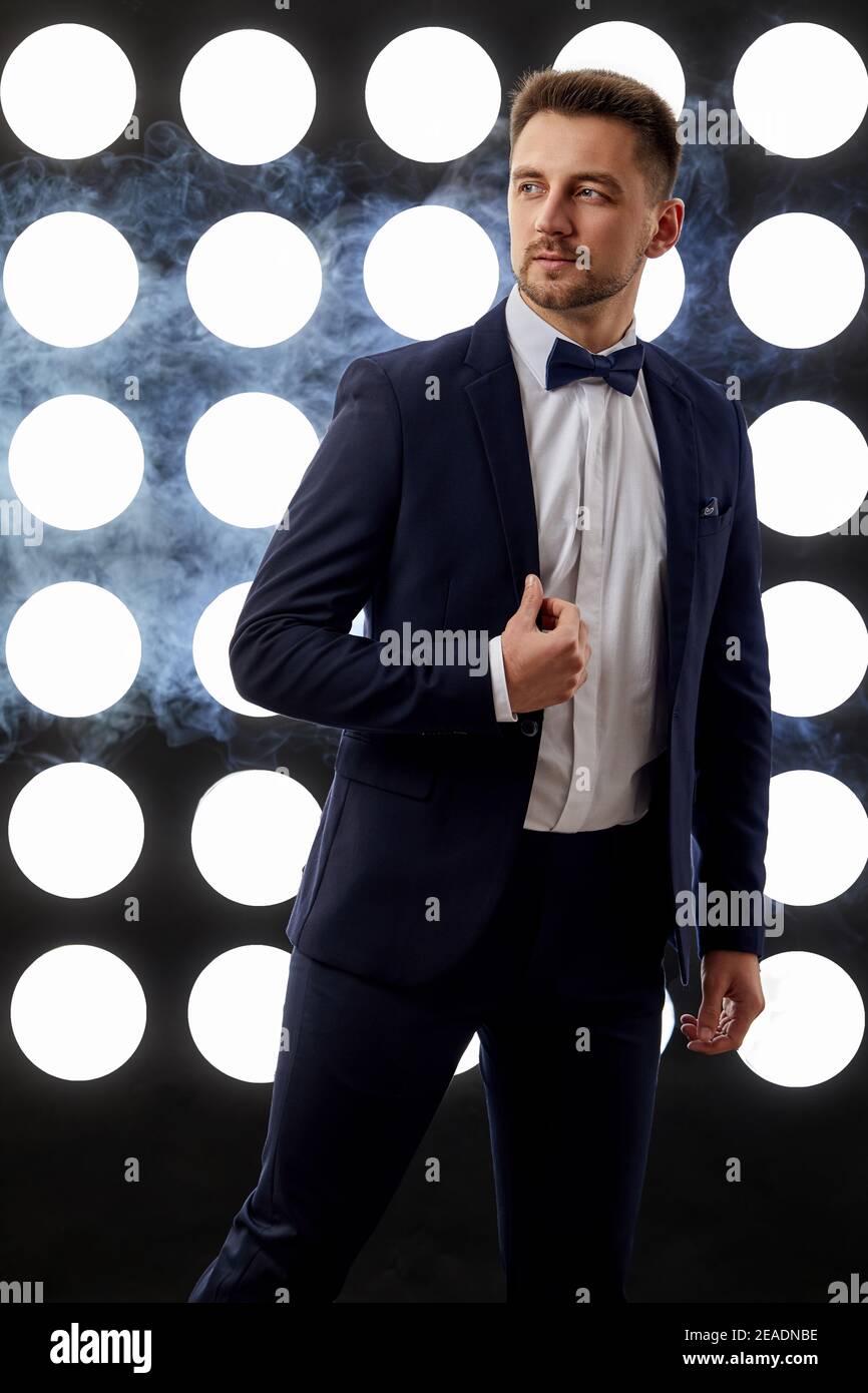 Schöner Mann im Smoking posiert vor dem Hintergrund von Scheinwerfern und Rauch. Nachtleben Stockfoto