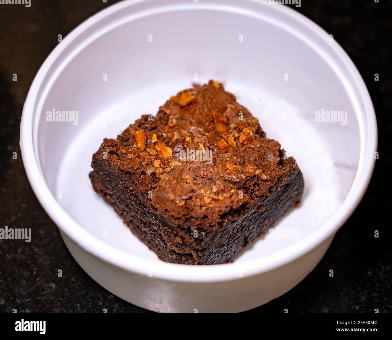 Nahaufnahme eines Brownie aus Schokoladenalmond in einer weißen Takeout-Box auf schwarzem Granit-Hintergrund. Stockfoto