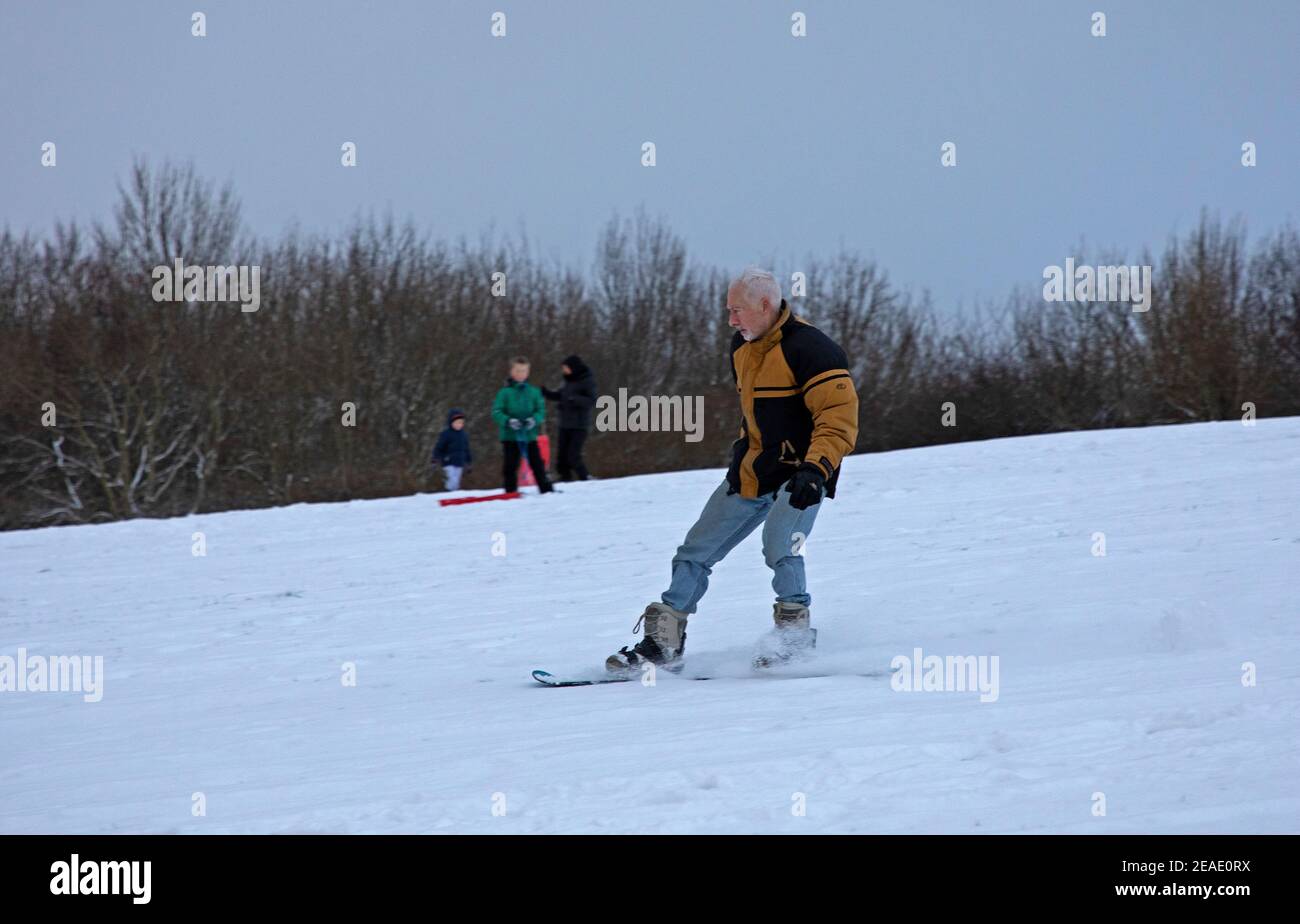 Holyrood Park Edinburgh, Schottland, Großbritannien. 9th. Februar 2021. Der schneebedeckte Holyrood Park ermutigte die Leute, zwischen den Duschen zu spielen und zu trainieren. Ältere Snowboarder genießen eine Abfahrt die Piste hinunter. Stockfoto