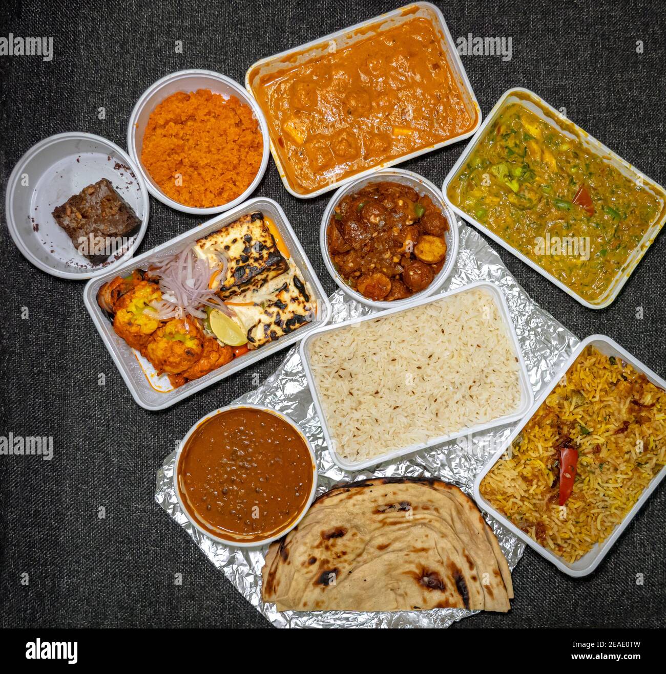 Draufsicht auf eine Vielzahl von indischen Speisen zum Mitnehmen in Plastikbehältern auf einem Stoffhintergrund. Stockfoto