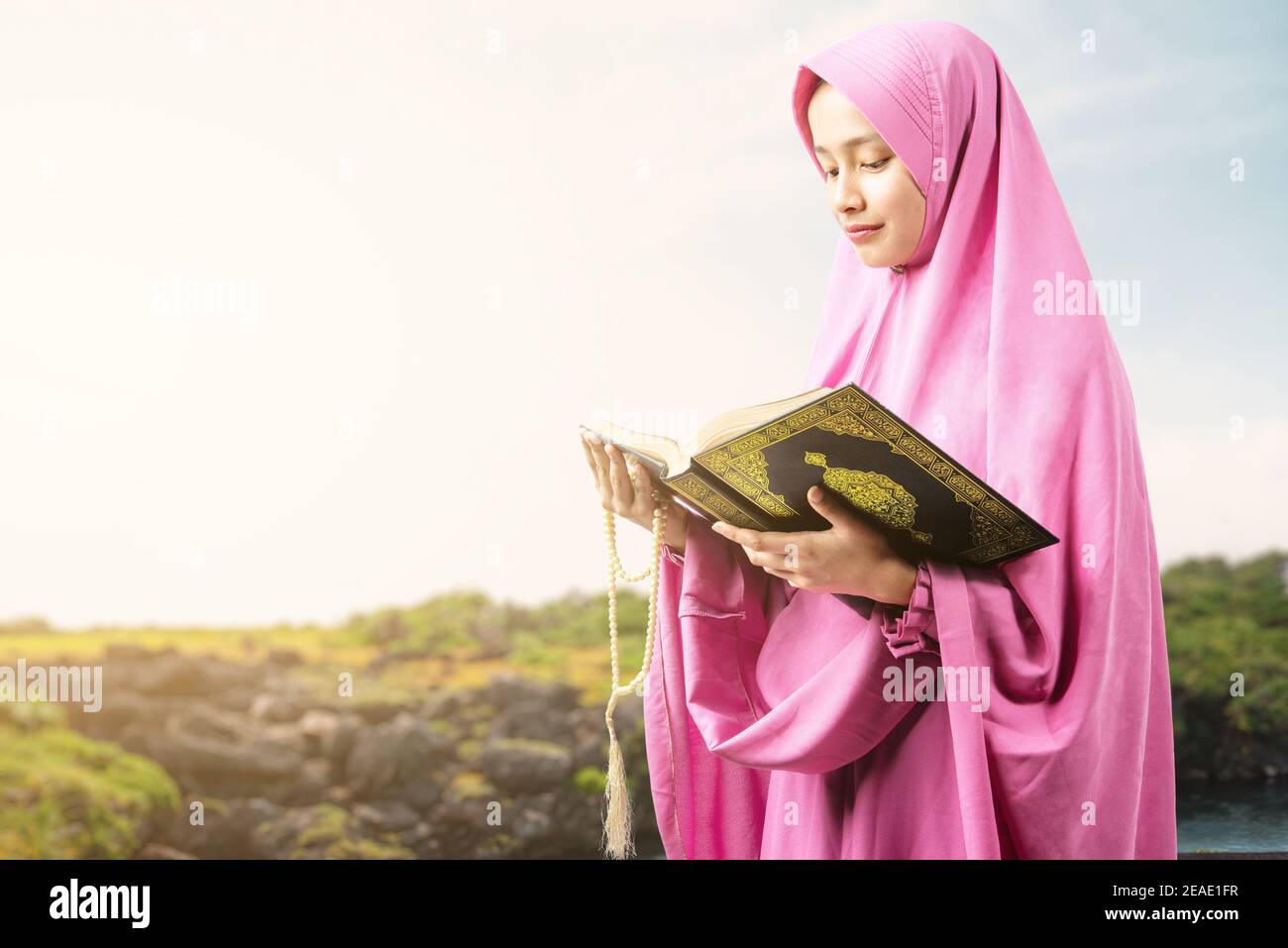 Asiatische muslimische Frau in einem Schleier hält Gebetsperlen und Lesen des Quran im Freien Stockfoto