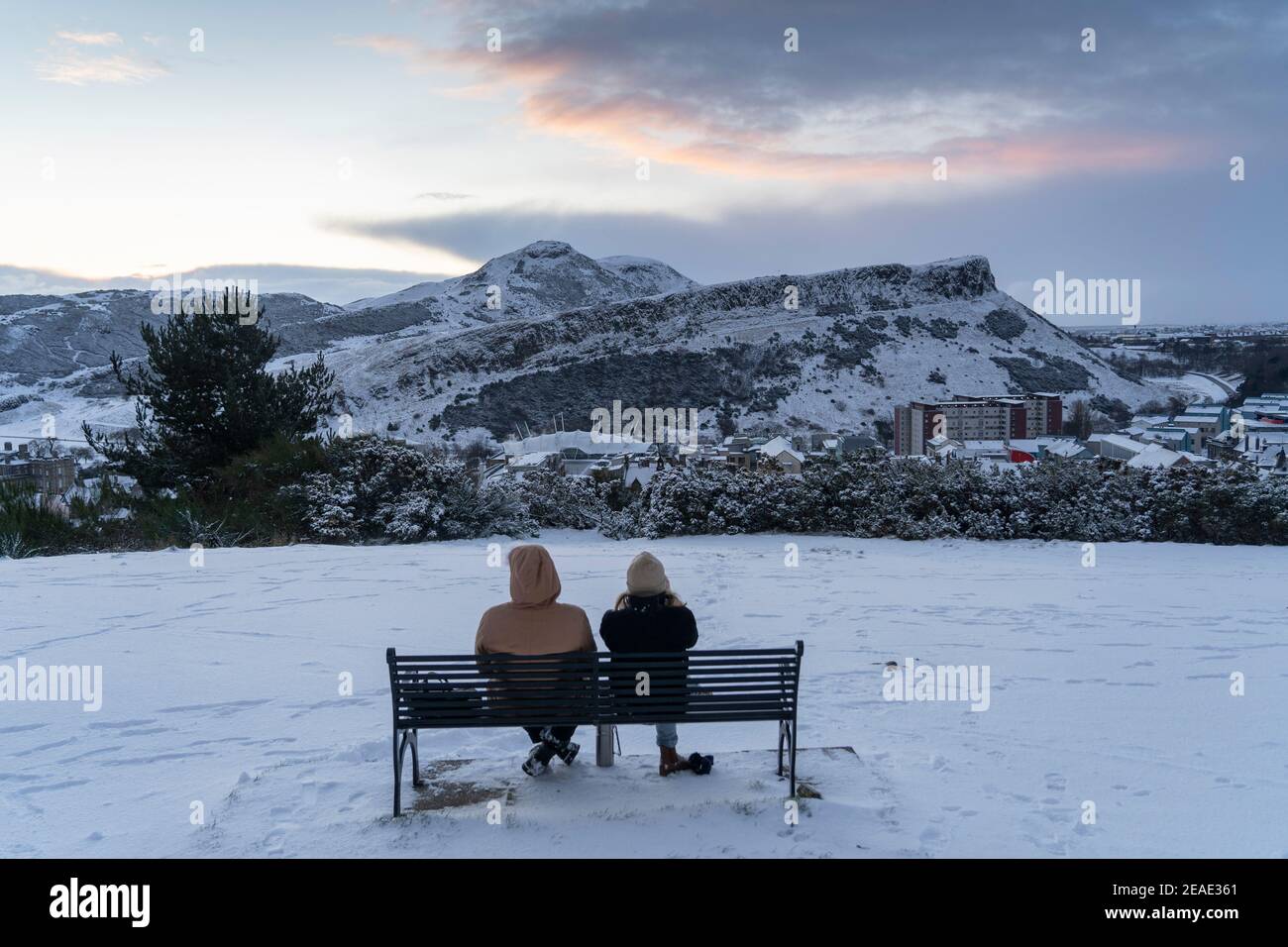 Edinburgh, Schottland, Großbritannien. Februar 2021, 9. Der große Frost geht in Großbritannien weiter, während Storm Darcy über Nacht mehrere Zentimeter Schnee nach Edinburgh bringt. PIC; Paar beobachten Sonnenaufgang über Salisbury Crags und Arthur's Seat. Iain Masterton/Alamy Live Nachrichten Stockfoto