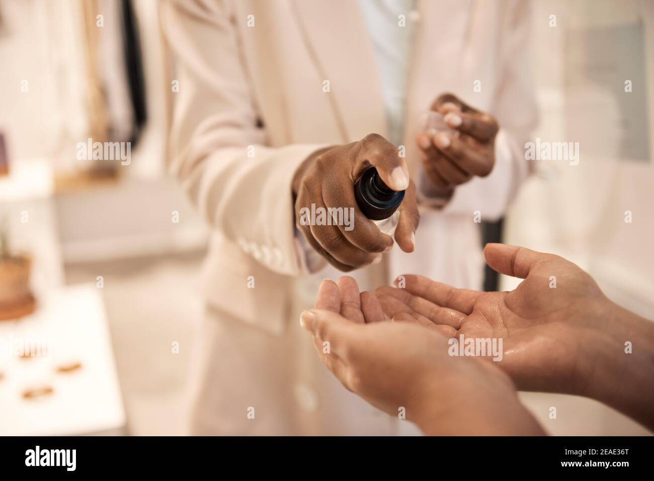 Afroamerikanischer Ladenbesitzer, der einem Kunden die Hände mit Desinfektionsmittel sprüht Stockfoto