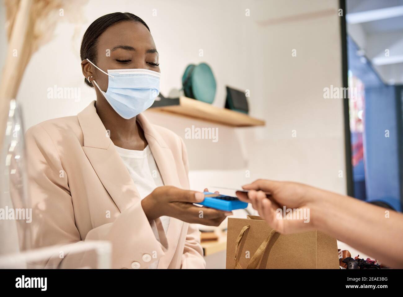 Afroamerikanischer Unternehmer in einer Maske, die eine kontaktlose Karte nimmt Zahlung Stockfoto