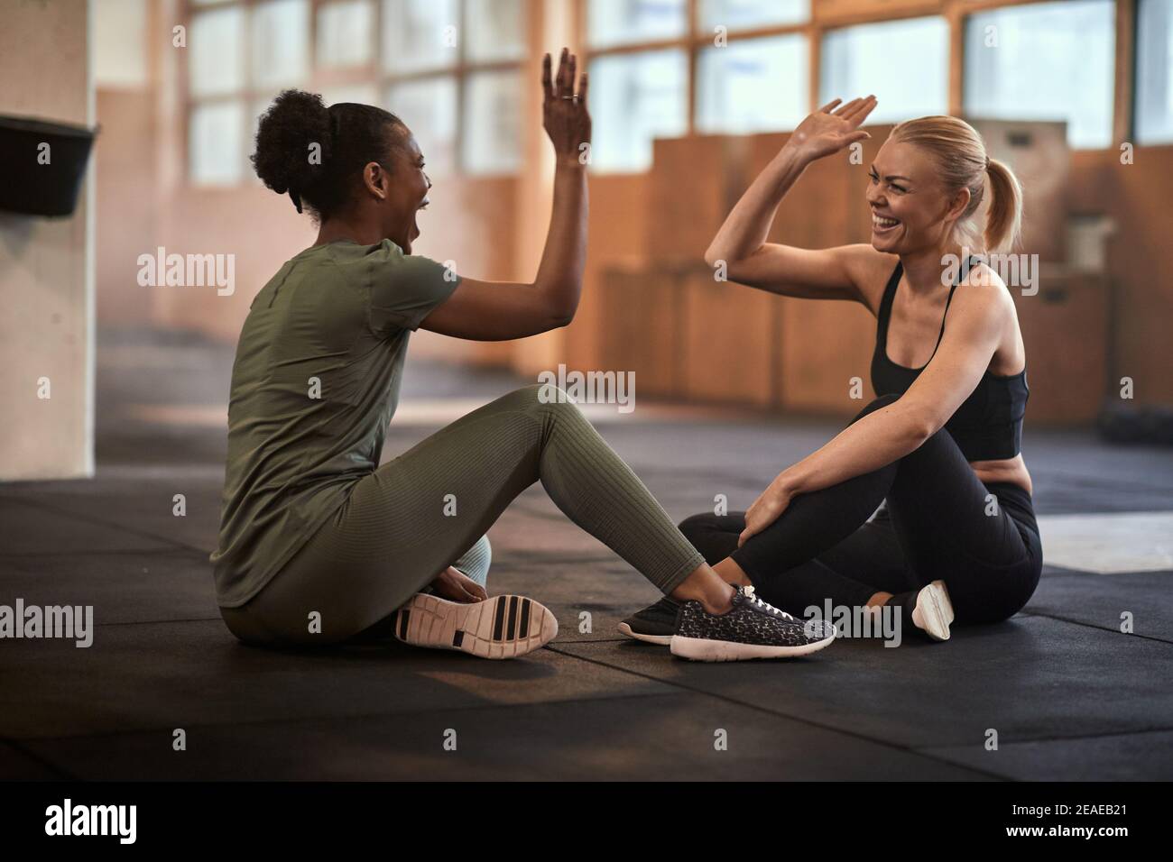 Zwei junge Frauen, die beim Sitzen lachen und sich hochkneifen Nach dem Training auf der Fitnessetage Stockfoto