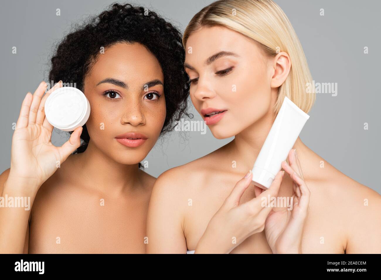 Multiethnische Frauen mit perfekter Haut posiert mit kosmetischen Creme isoliert Auf Grau Stockfoto