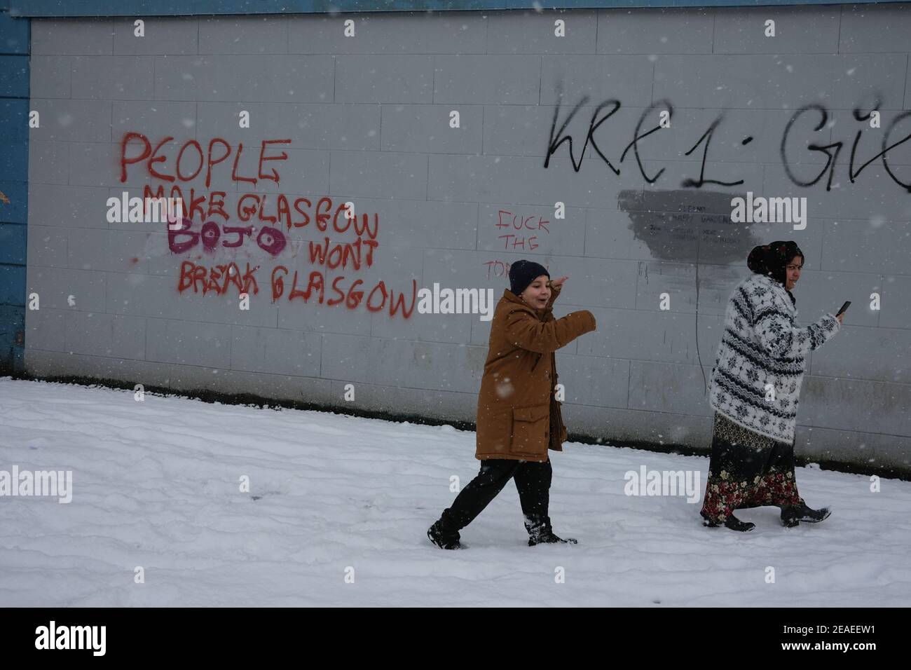 Glasgow, Großbritannien, am 9. Februar 2021. Eine rumänische Roma-Mutter und ihr Sohn gehen an Graffiti vorbei, das besagt: "Menschen machen Glasgow, Bo(ris) Jo(hnson) will't break Glasgow", im Schnee, der über Nacht fiel. Foto: Jeremy Sutton-Hibbert/ Alamy Live News. Stockfoto