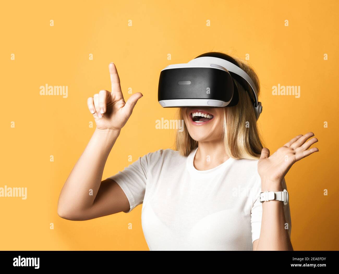 Happy blonde Frau in weißem T-Shirt verwendet VR-Brille erkundet Augmented Reality Drücken der virtuellen Taste mit dem Finger Stockfoto