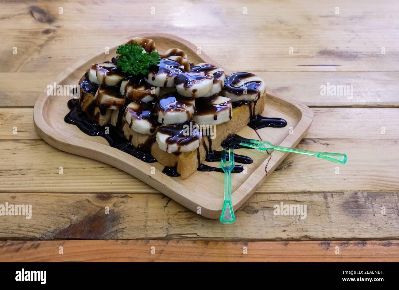 Getoastetes Brot mit geschnittenen Bananen und mit Schokoladensauce auf einem Holztablett auf einem Holztisch, Vorderansicht mit dem Kopierraum platziert gekrönt. Stockfoto