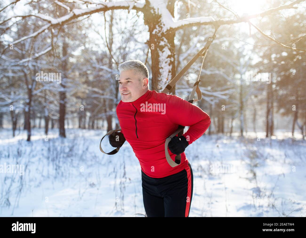 Funktionstraining. Porträt eines älteren Mannes, der im Winter mit Fitnessbändern im verschneiten Park Übungen macht Stockfoto