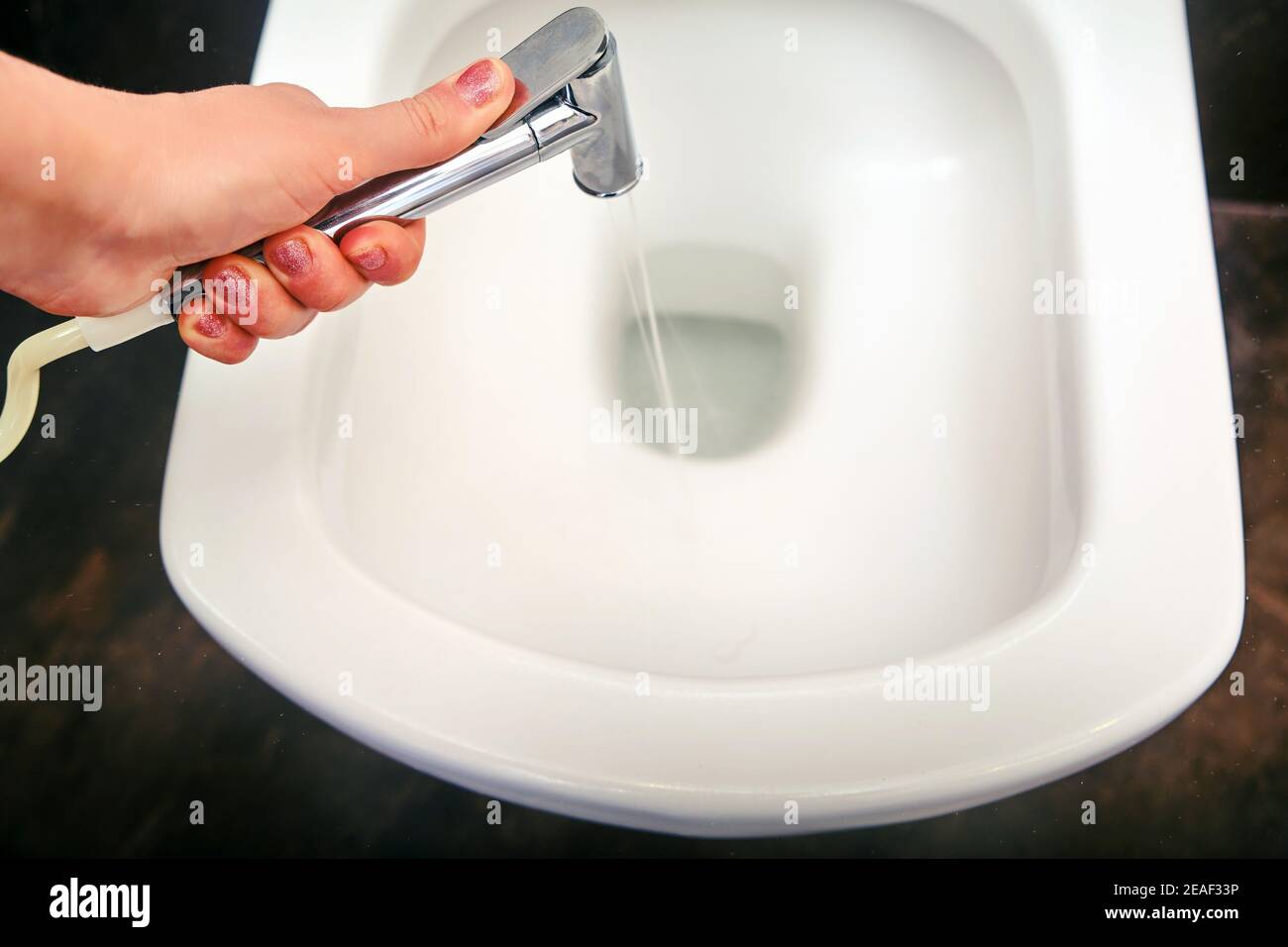 Eine Frau wäscht Toilettenschüssel mit einer hygienischen Dusche, Nahaufnahme. Probleme mit der Desinfektion durch Quarantäne und Isolation von Coronavirus. Brauner Stein Stockfoto