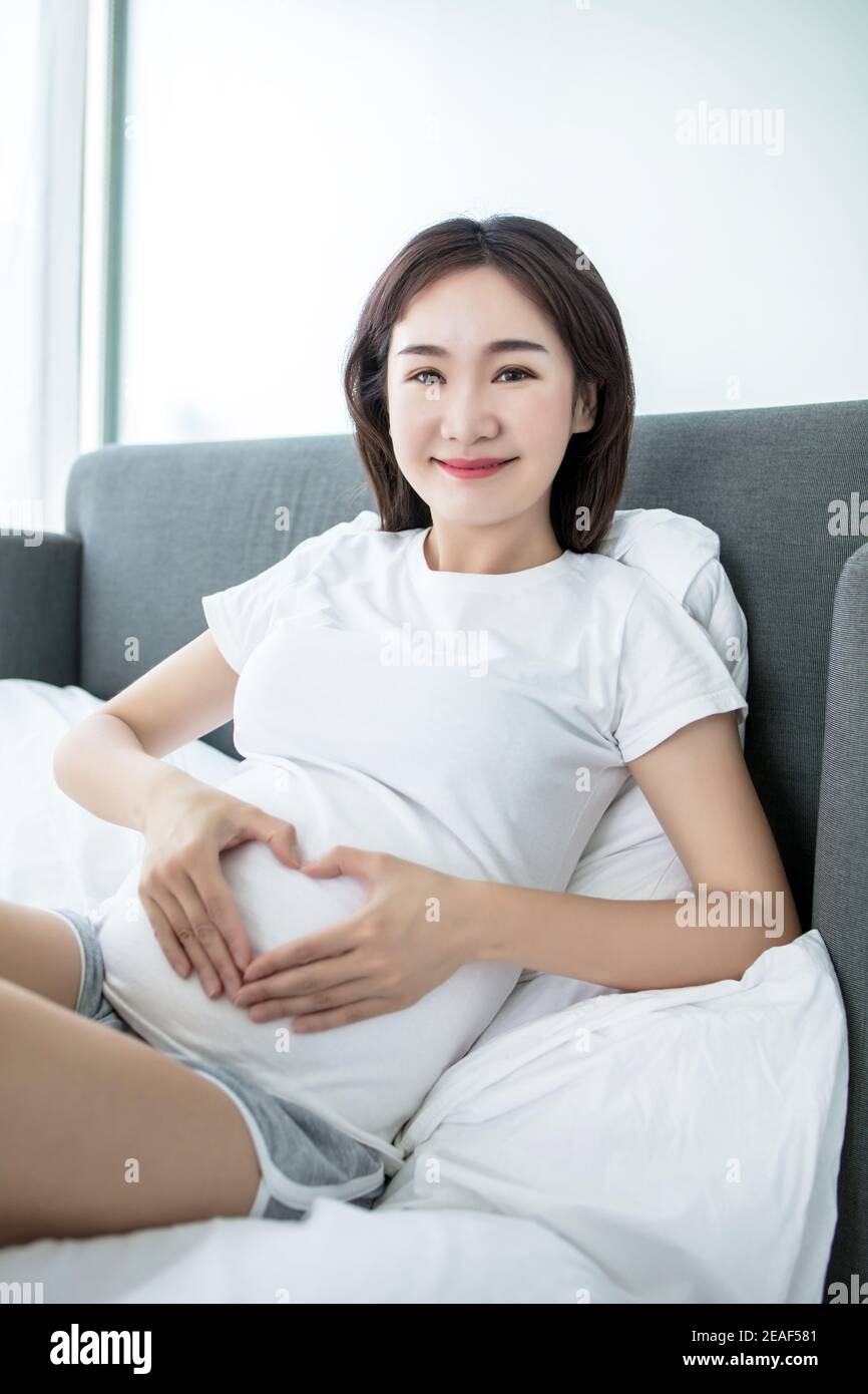 Schwangerschaft, Liebe, Menschen und Erwartung Konzept - glücklich  schwangere asiatische Frau im Bett sitzen und machen Hand Herz Geste zu  Hause Stockfotografie - Alamy