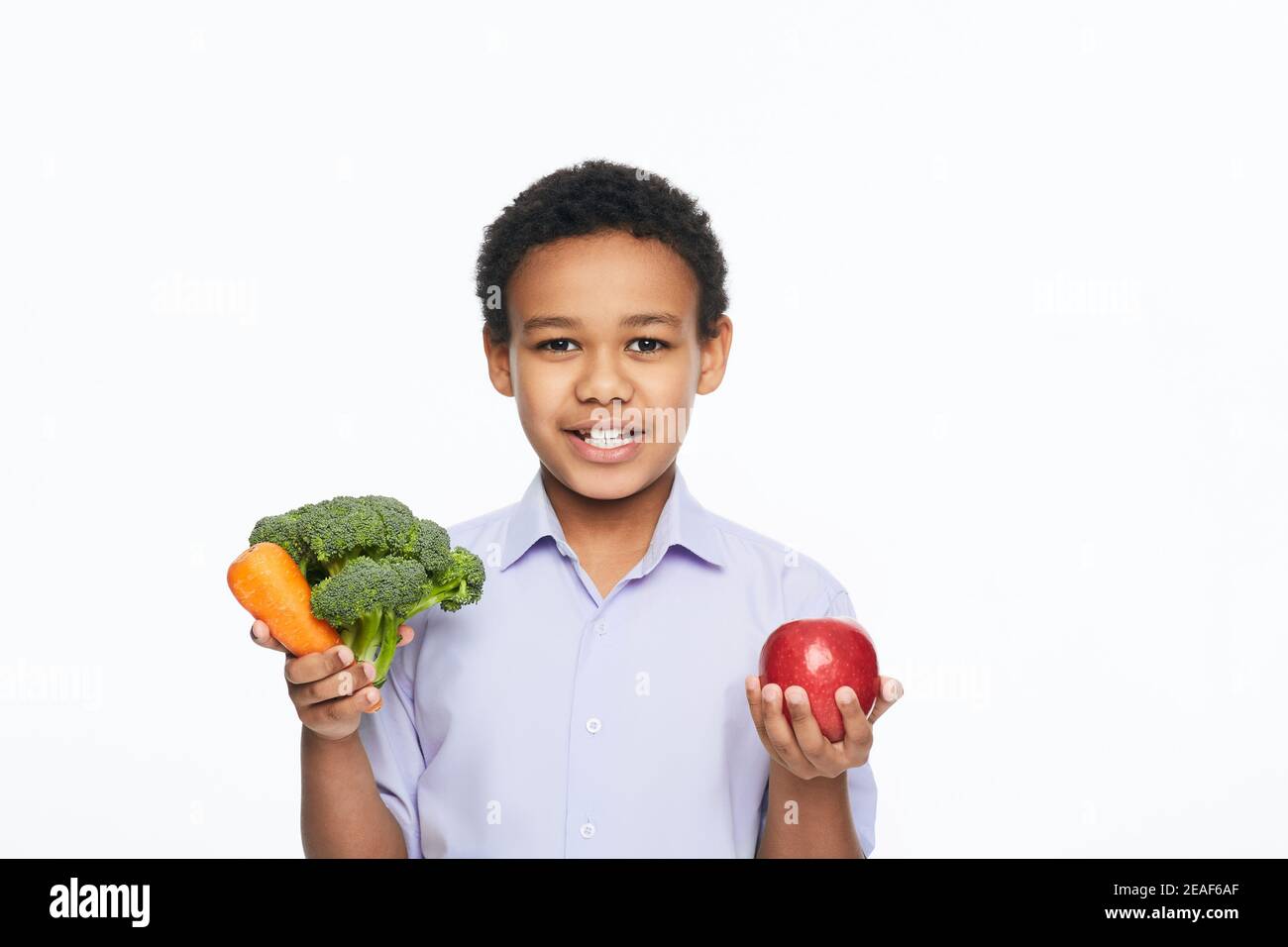 Afroamerikanischer Junge, der Gemüse und Früchte in der Hand hält. Gesundes vegetarisches Lebensmittelkonzept für Kinder Stockfoto