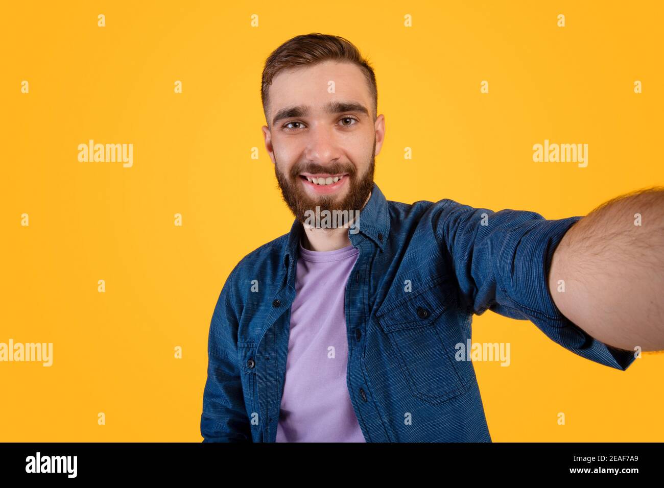 Schöner junger Kaukasischer Kerl, der Selfie nimmt und weit über lächelt Orangefarbener Studiohintergrund Stockfoto