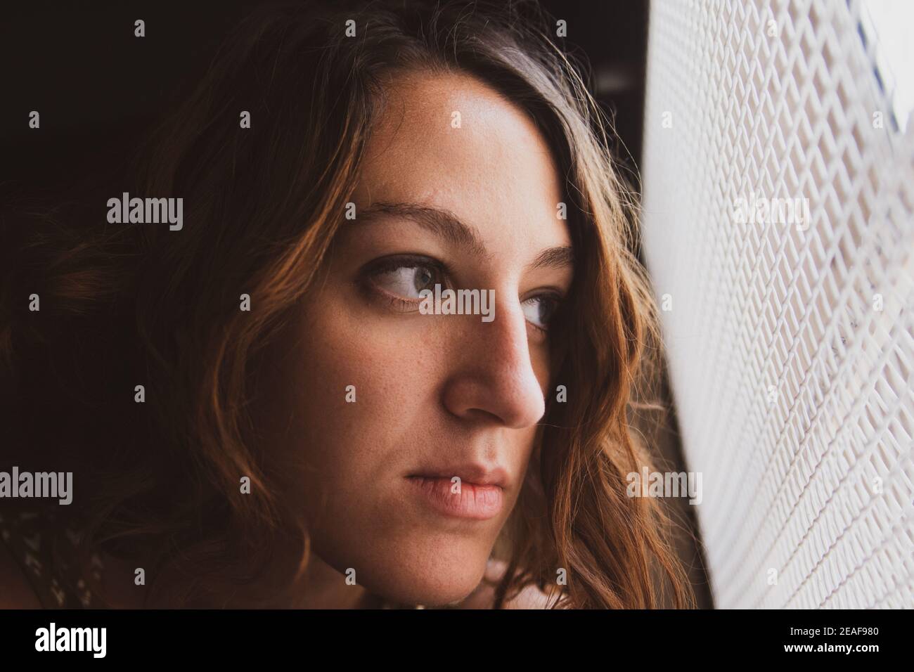 Traurige junge Frau, die aus dem Fenster schaute. Einengung in Zeiten des Coronavirus. Wunsch nach Ausgehen Stockfoto