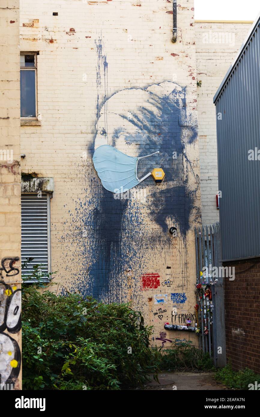 'The Girl with the Pierced Eardrum' Banksy malte einen Verbündeten in Bristol, England. Das Mädchen trägt eine Gesichtsmaske während der Covid Pandemie von 202 Stockfoto
