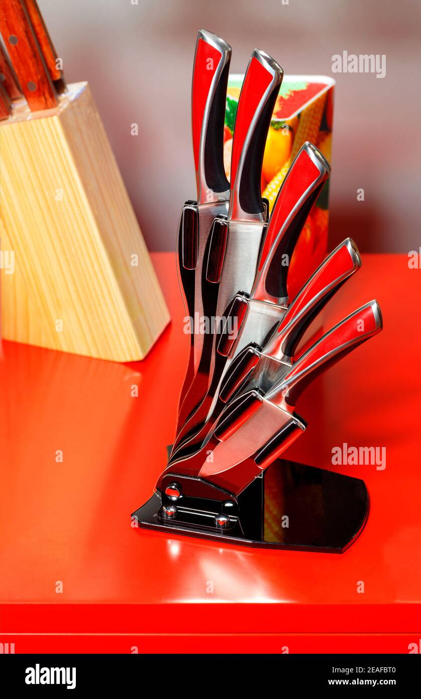 Ein Set aus schönen Küchenmessern aus Edelstahl in einem eleganten schwarzen Etui auf rotem Hintergrund. Stockfoto