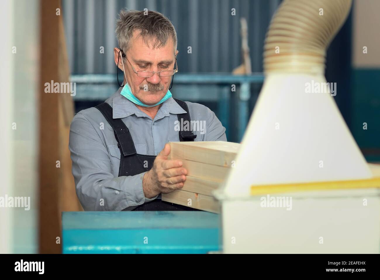 Ein älterer Zimmermann mit kaukasischem Aussehen arbeitet in einer Schreinerei. Die Bearbeitung der Bretter auf der Drehbank. Stockfoto