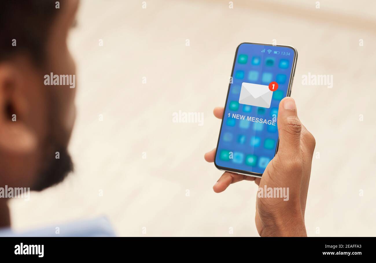 Black Guy Reading E-Mail Nachricht am Telefon sitzend Innen, abgeschnitten Stockfoto