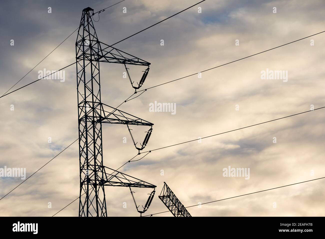 Ein Strommast auf der Basis eines Trassens gegen den Himmel und Wolken bei Sonnenuntergang gebaut. Stockfoto