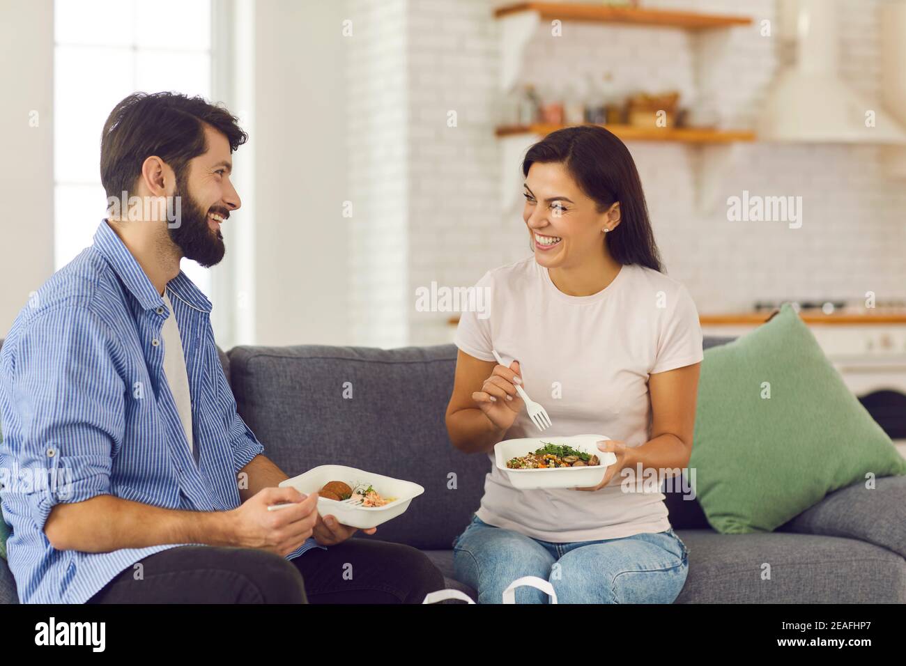 Junge lächelnde Paar Mann und Frau zu Hause sitzen und Essen gesunde Lebensmittel verpackt Stockfoto