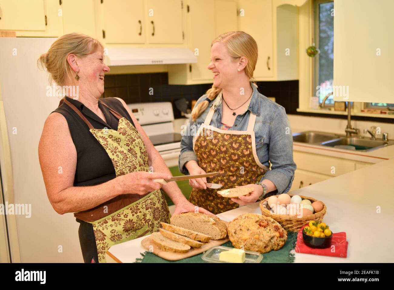 Zwei attraktive kaukasische Frauen Hausbäcker in Schürzen, schneiden frisch gebackenes Brot auf der Küchentheke, Butter Brot, Wisconsin, USA Stockfoto