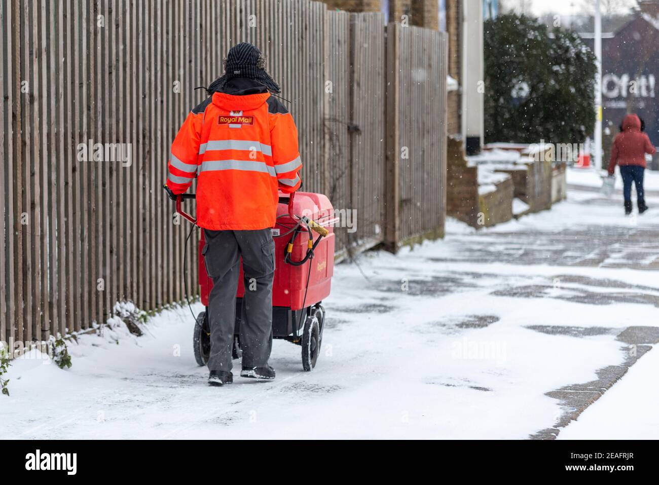 Royal Mail Postarbeiter schiebt einen Postwagen in Southend on Sea, Essex, Großbritannien, mit Schnee von Storm Darcy. Eisige Straßenverhältnisse. Weitermachen Stockfoto