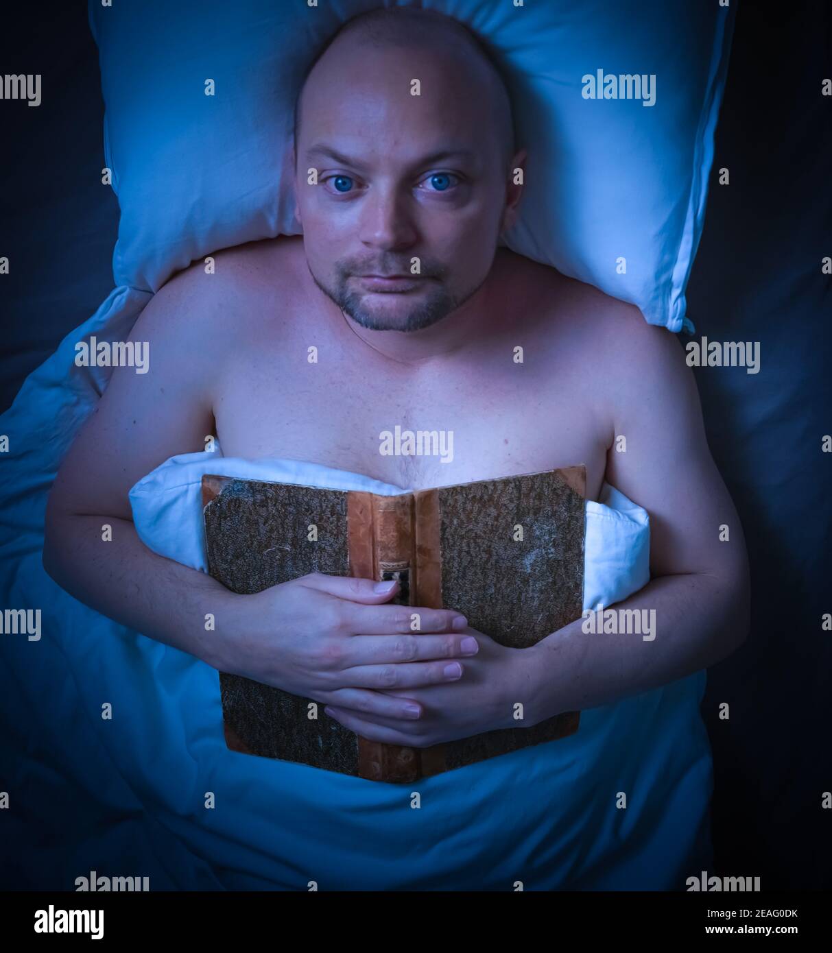 Mann, der im Bett lag und ein Buch sah nachdenklich aus. Stockfoto