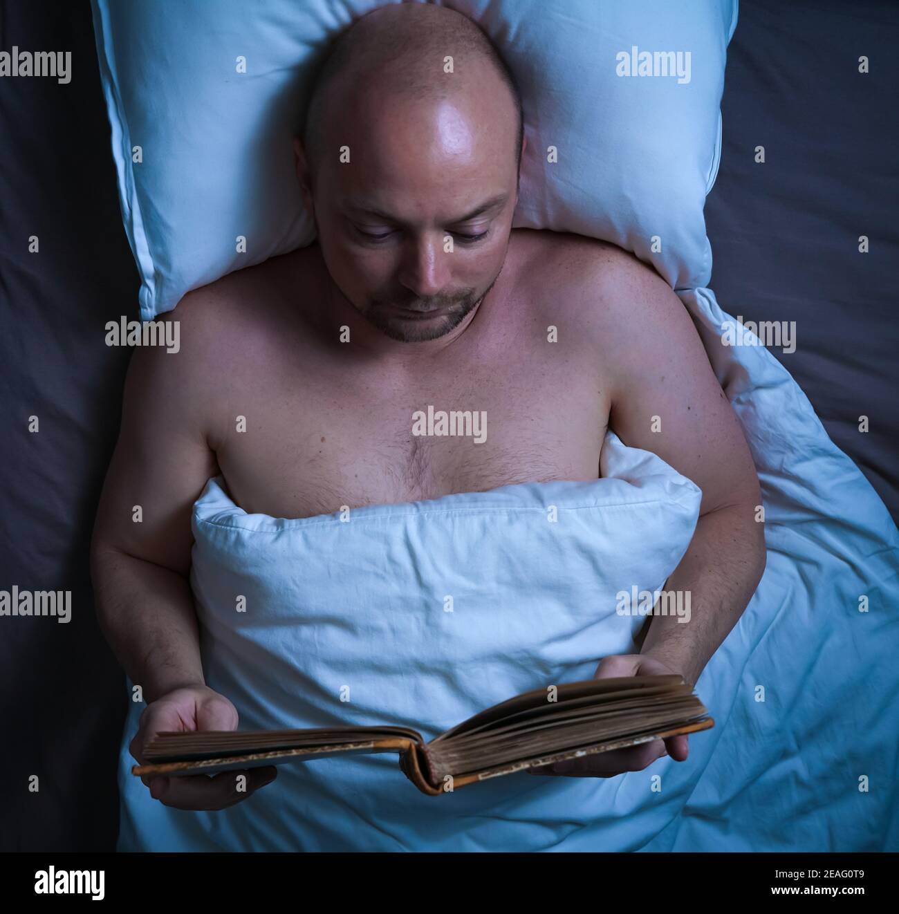 Mann liest nachts ein Buch im Bett. Stockfoto