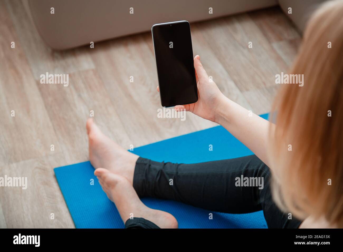 Mockup für App Online-Fitness-Programm, Remote Yoga-Klasse. Frau in Sportswear hält Smartphone mit leerem Bildschirm für Sport oder Musik App während ein Stockfoto