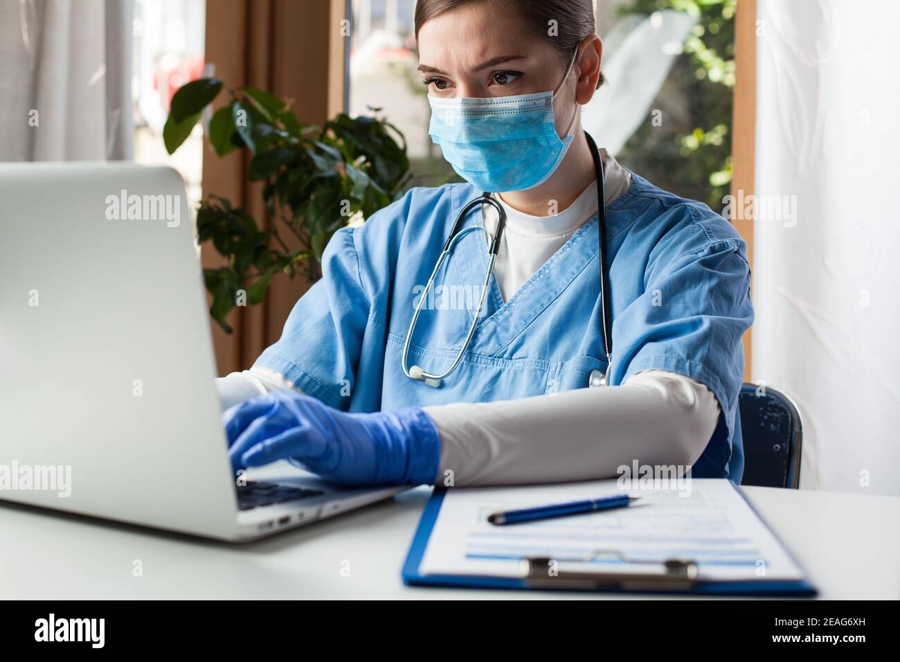 Junge kaukasische Ärztin, die im Büro am Laptop-Computer arbeitet Schutzhandschuh und Gesichtsmaske, Electronic Medical Records EMR-Konzept Stockfoto