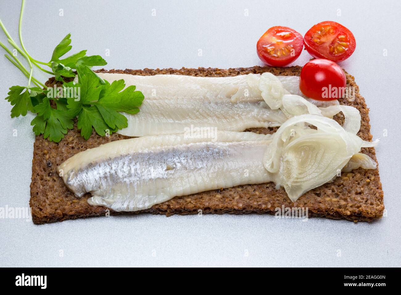 Filets von eingelegtem Hering auf Roggenbrot, mit Zwiebeln, Tomaten und Petersilie. Stockfoto