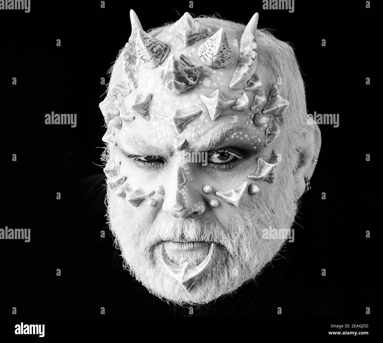 Teufel mit runzelndem Gesicht und weißen Augen. Böse mit Drachenhaut und Bart. Alien oder Reptilien Make-up mit Dornen und Warzen. Dämonenkopf auf schwarz Stockfoto