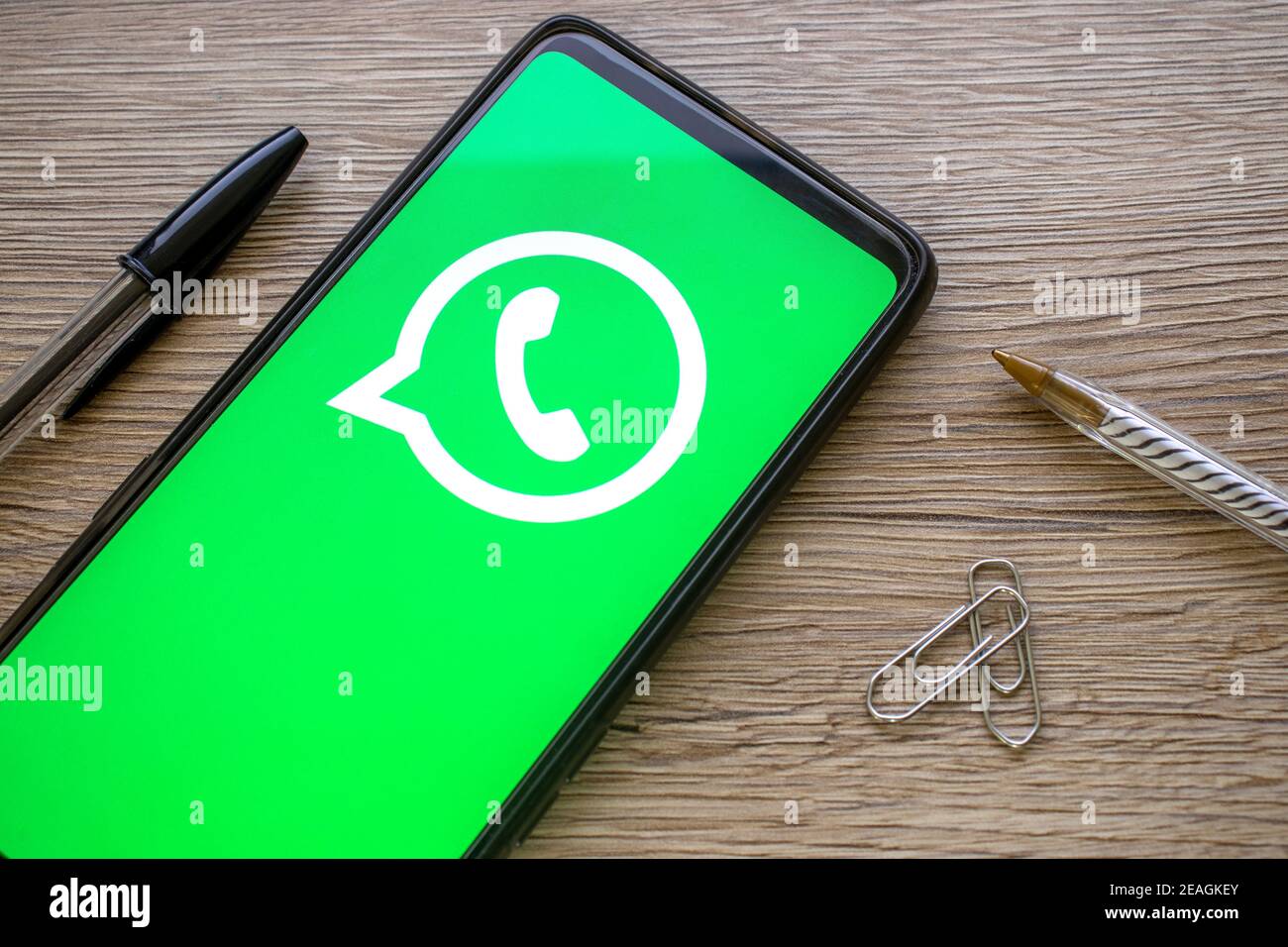 Smartphone mit grünem whatsapp-Logo auf Holztisch mit Stift-Büroklammern. Telefon-Datenschutz-Konzept mit Zuckerberg Social Media-Symbol. Stockfoto