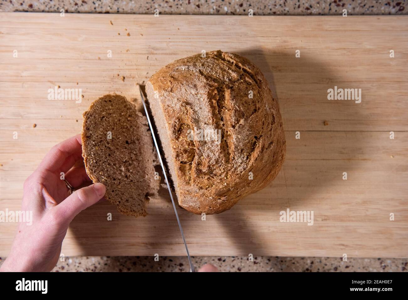 Ein frisch gebackenes Brot wird in Scheiben geschnitten. Serie Schritt-für-Schritt Herstellung hausgemachtes Brot. Bild 12 von 13 Stockfoto