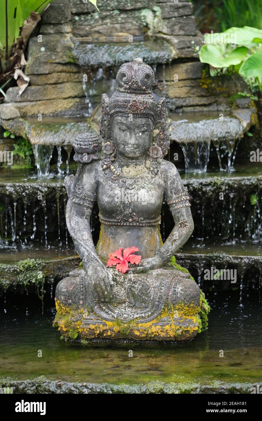 Indonesien Bali - Ubud Handgefertigte balinesische Steinstatue mit Hibiskus Blume vertikal Stockfoto