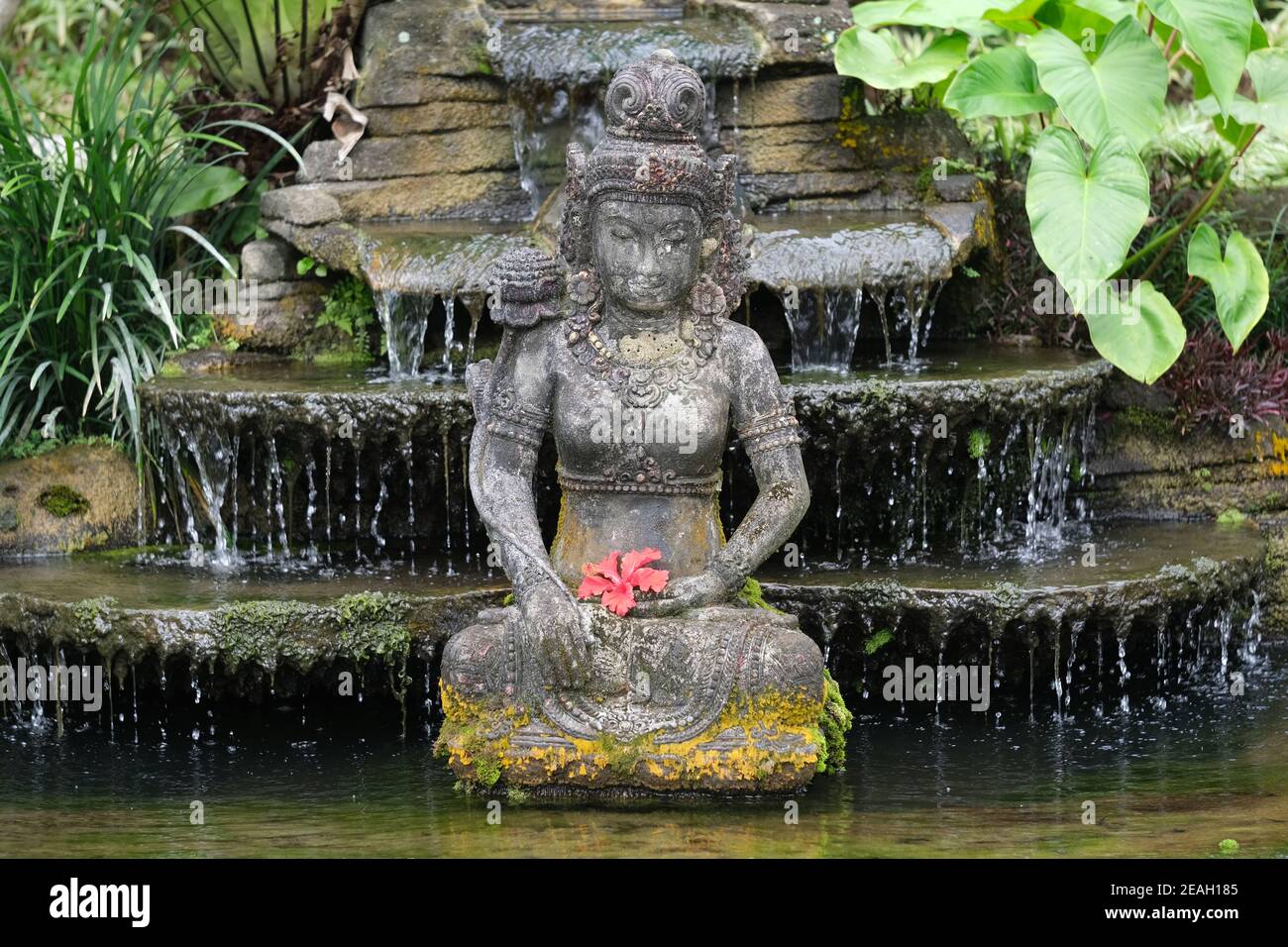 Indonesien Bali - Ubud Handgefertigte balinesische Steinstatue mit rot Hibiskusblüte Stockfoto