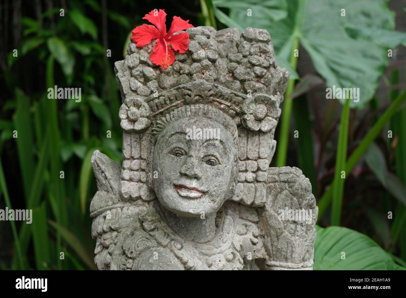 Indonesien Bali - Ubud Handgefertigte balinesische Steinstatue mit rot Hibiskusblüte Stockfoto