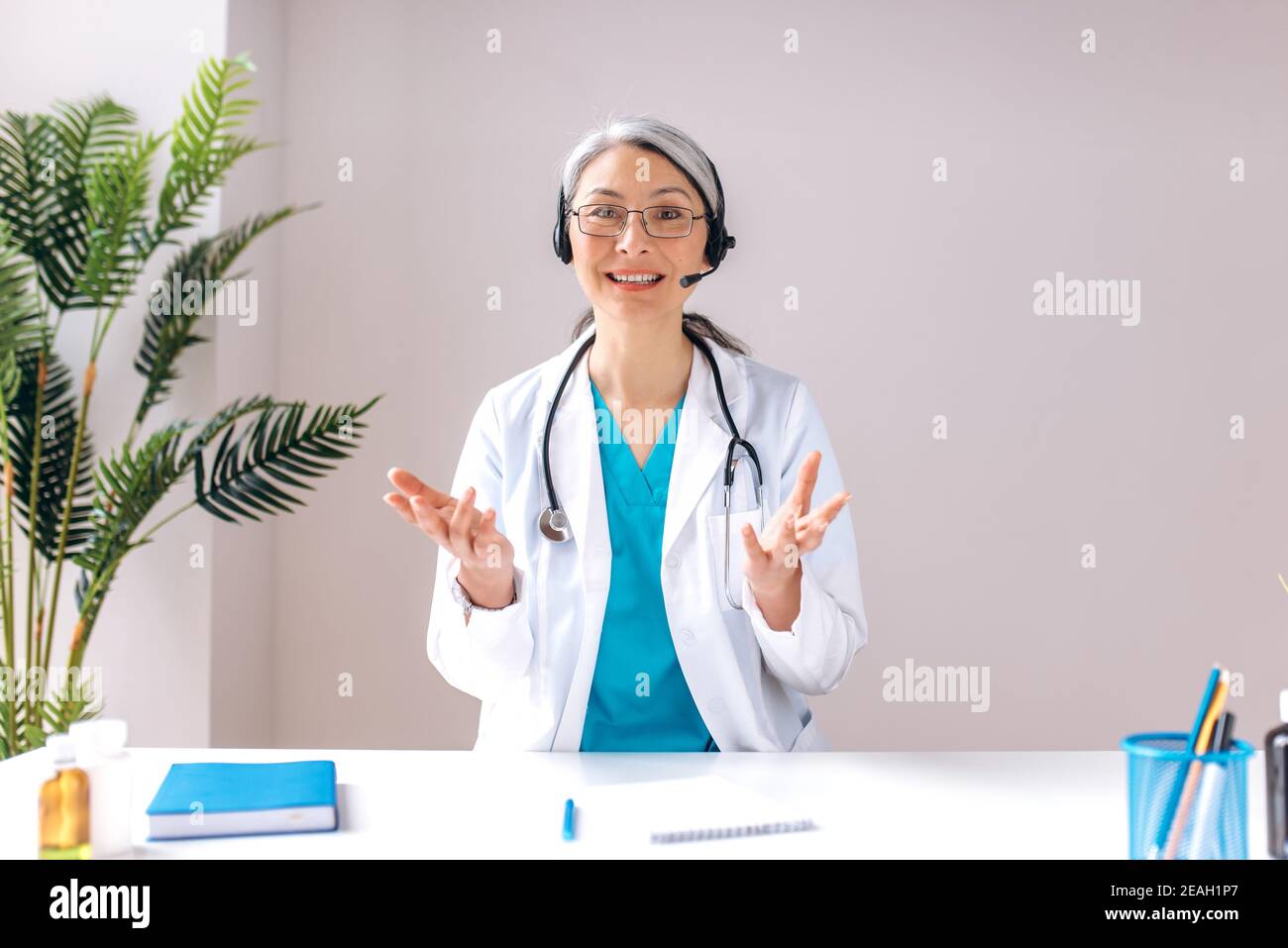 Eine freundliche ältere grauhaarige Ärztin trägt ein Headset und schaut auf die Kamera und lächelt. Remote-Online-medizinische Beratung, Medizin Ferndienste, virtuelle medizinische Hilfe Konzept Stockfoto