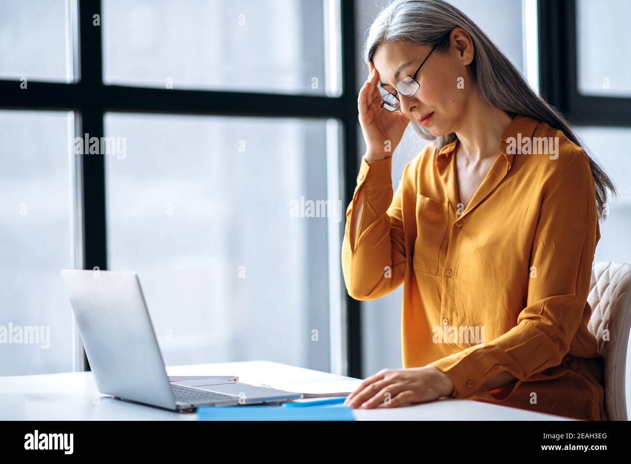 Frustriert asiatische Senior grauhaarige Geschäftsfrau oder Tutor, ist müde nutzt Laptop für die Online-Arbeit, oder führen Abstand Lehre, schloss ihre Augen, Kopfschmerzen, brauchen eine Pause Stockfoto