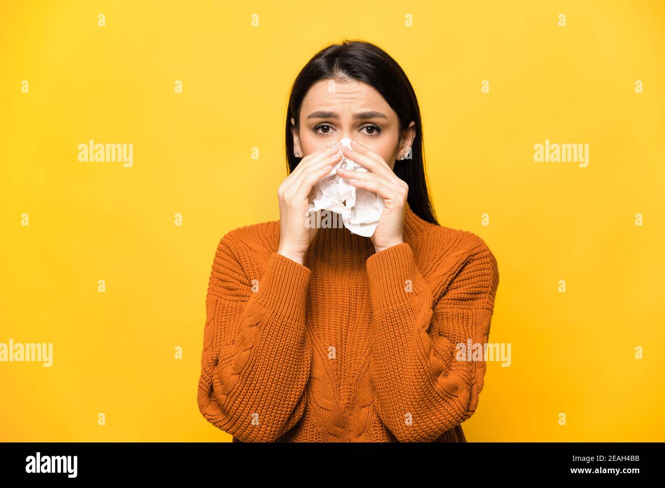 Ungesunde traurig kaukasische junge Erwachsene Brünette Mädchen auf einem isolierten gelben Hintergrund Niesen in ein Taschentuch, Grippe, Erkältung, Virus. Medizin und Gesundheitswesen Konzept Stockfoto