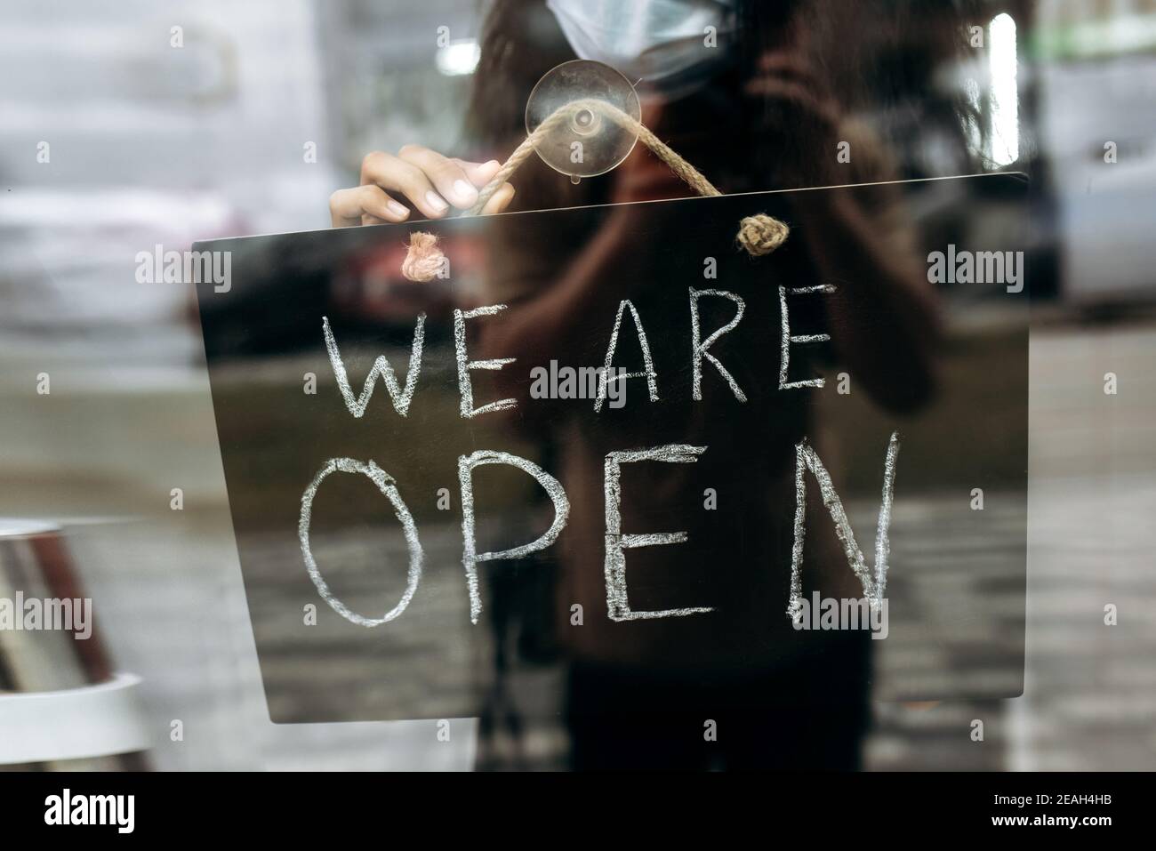 Nahaufnahme Foto von einem Schild SIND WIR AM Eingang zu einem Restaurant oder Café geöffnet. Weibliche Hand hält Schild OFFEN am Eingang zu einem Restaurant, Bar, Café oder Shop Stockfoto