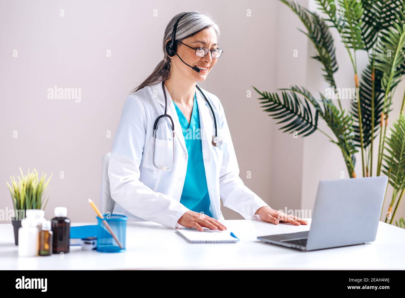 Ärztin mittleren Alters Arzt trägt einen Laborkittel und Headset Sprechen per Videoanruf mit Laptop mit ungesunden Patienten, Online-Beratung. Konzept der medizinischen Fernhilfe Stockfoto