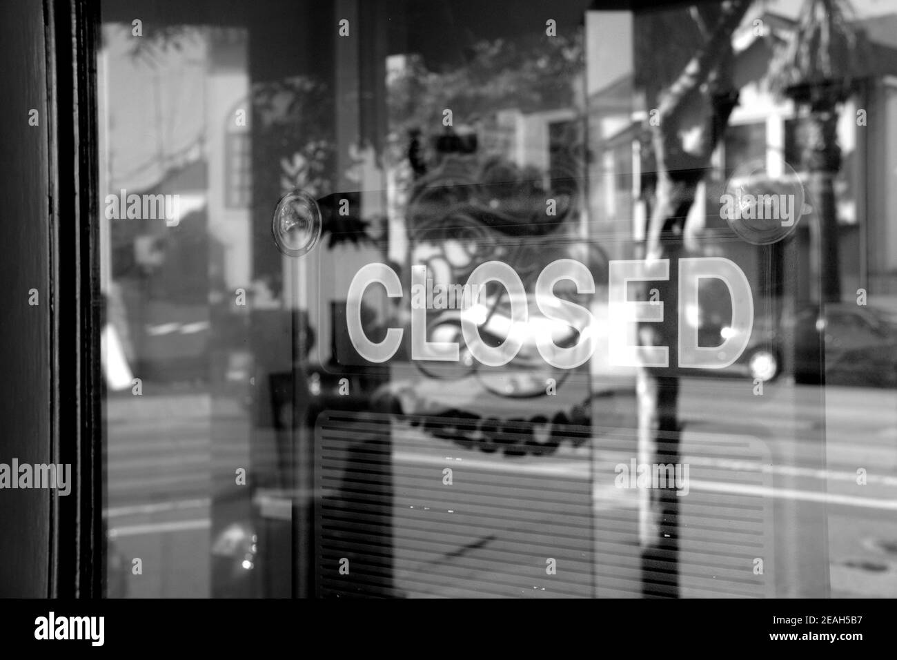Geschlossenes Schild durch eine Glastür mit Straßenspiegelung für stilisierten Effekt eingefangen gesehen; monochrom, schwarz und weiß. Stockfoto