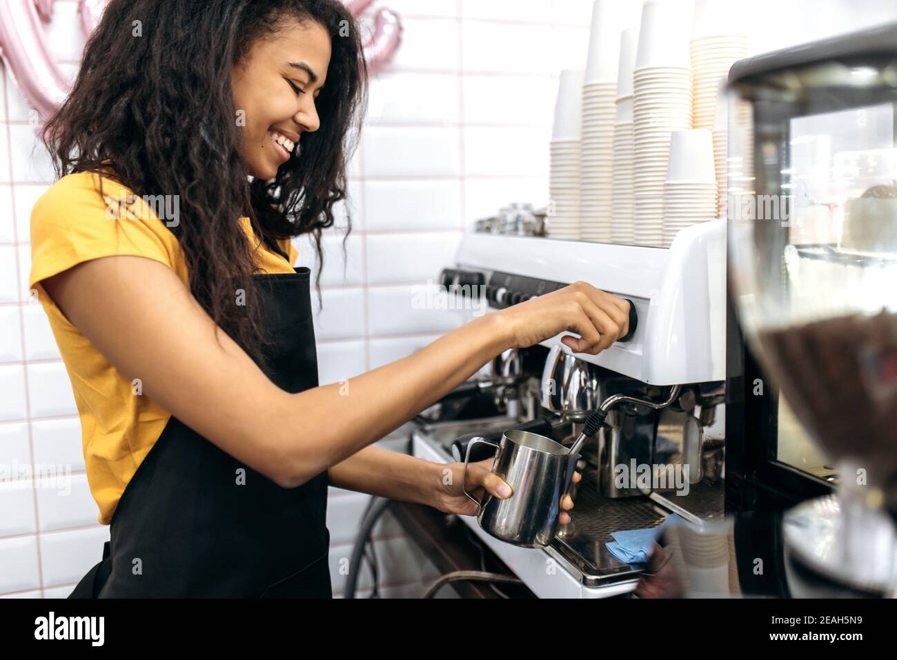 Lächelnde afroamerikanische Barista in Uniform macht Kaffee für einen Café-Besucher. Café, Konzept für kleine Unternehmen Stockfoto