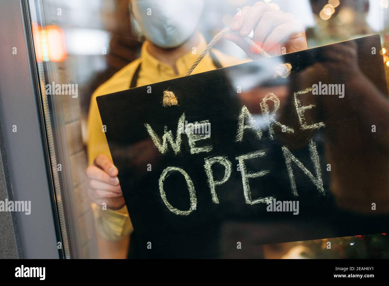 Nahaufnahme eines Schildes, DAS AM Eingang zu einem Restaurant oder Café geöffnet ist. Männliche Hand hält Schild OFFEN am Eingang zu einem Restaurant, Bar, Café oder Shop Stockfoto