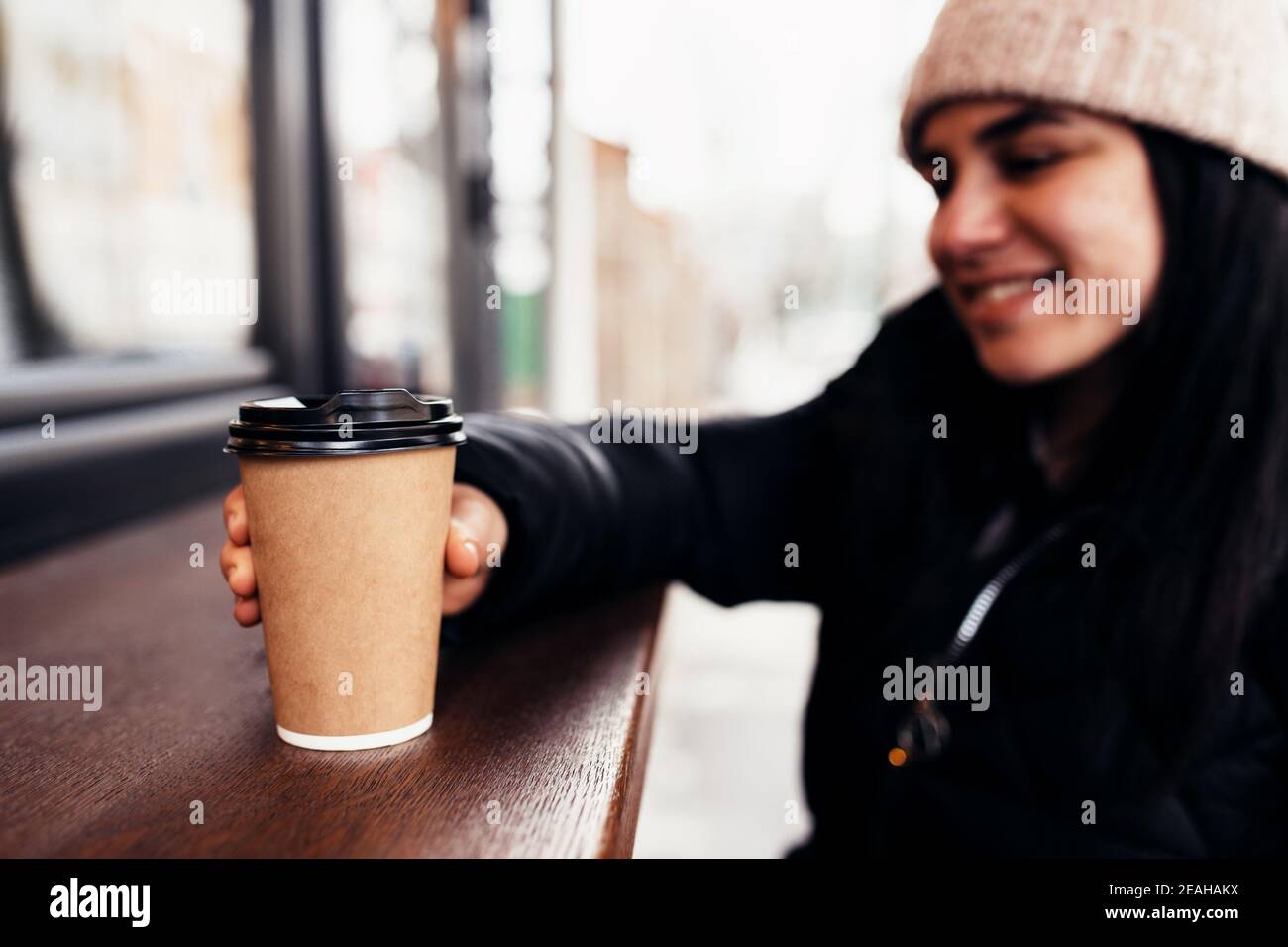 Mädchen lächelt, hält Papiertasse Kaffee in der Hand in der Nähe des Cafés. Unscharfer Hintergrund Stockfoto